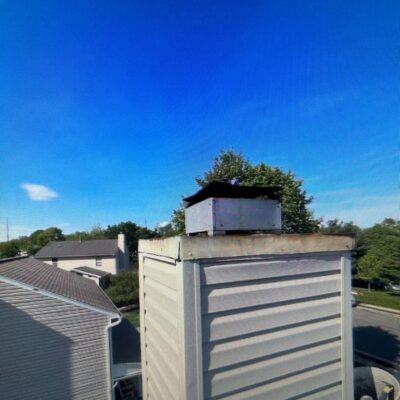 A new metal chase cover on a chimney with houses in the background and a clear blue sky.