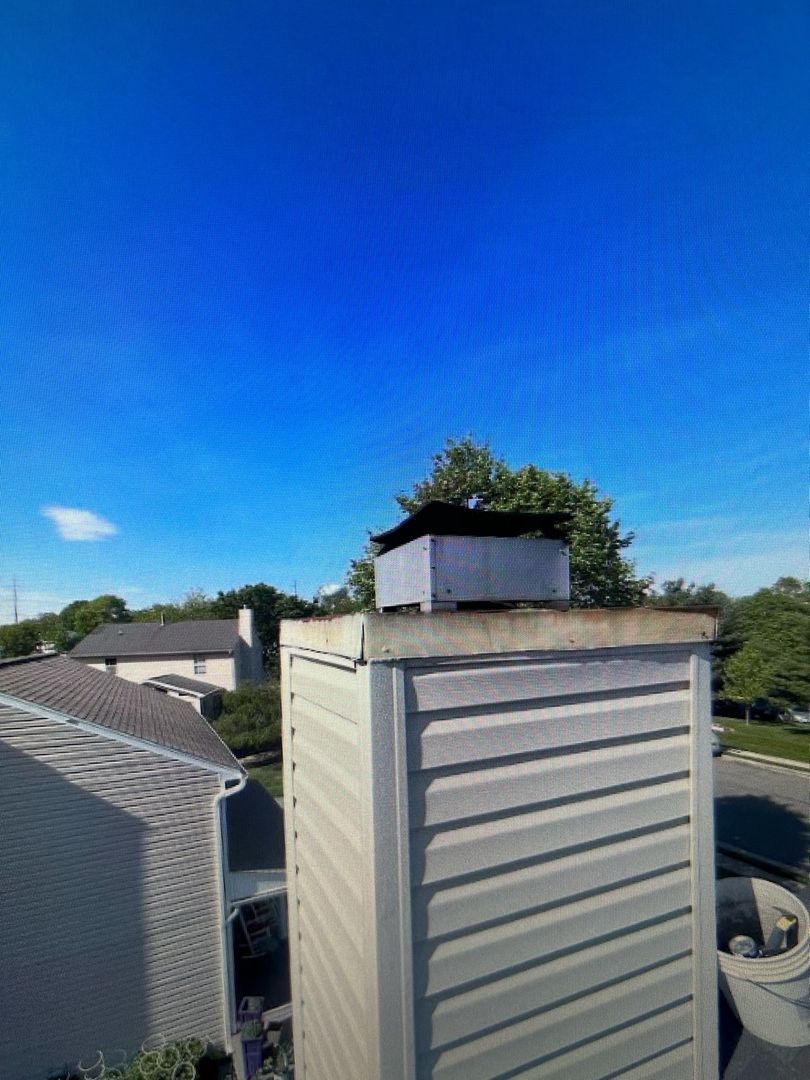 A new metal chase cover on a chimney with houses in the background and a clear blue sky.