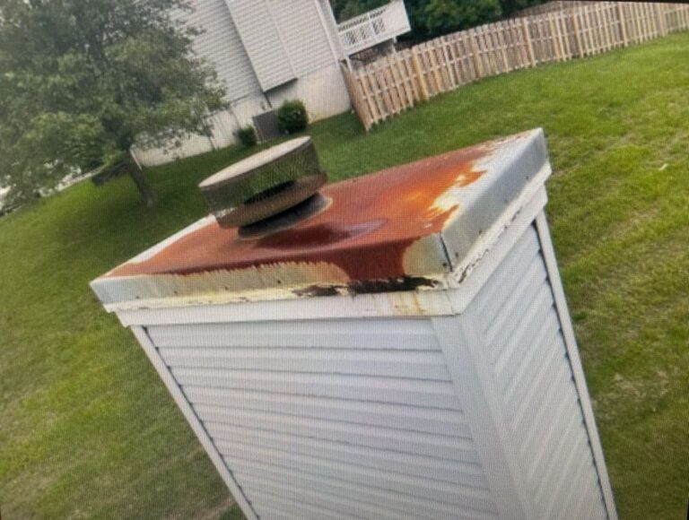 A rusty chase cover on top of a chimney in a residential yard indicating the need for maintenance.