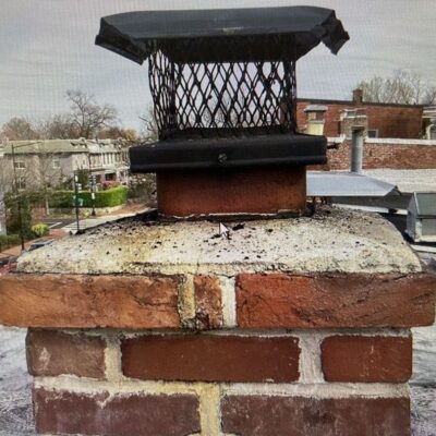 Chimney cap and crown on a brick chimney showing signs of wear against an urban backdrop
