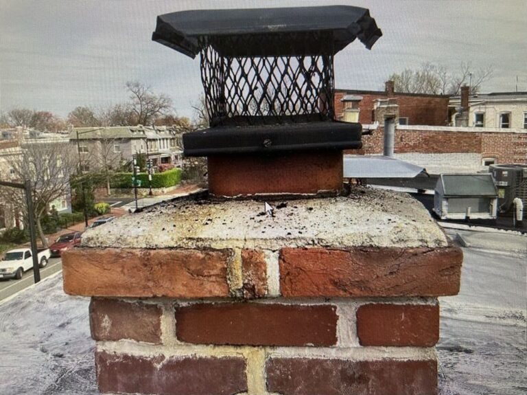 Chimney cap and crown on a brick chimney showing signs of wear against an urban backdrop