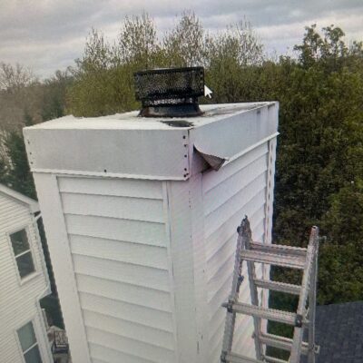 White chimney with damaged chase cover and ladder positioned for repairs.