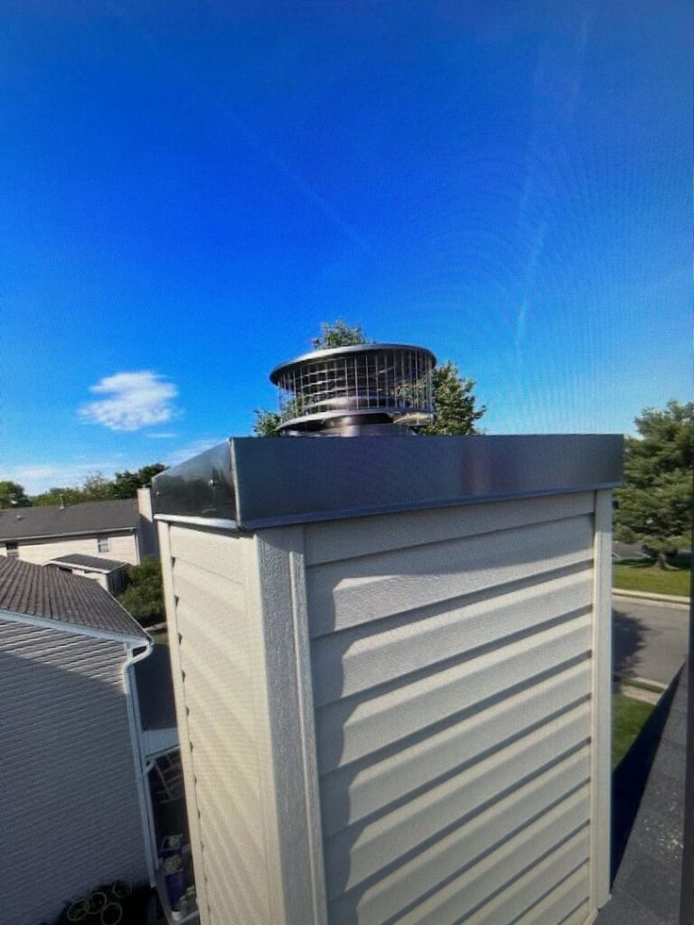 Newly installed chase cover and chimney cap with animal-proof screen on a residential roof.