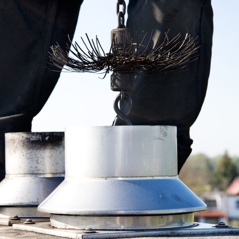 a chimney sweep lowering a brushing tool into a metal flue pipe