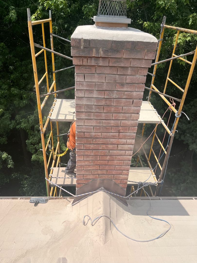 Worker on scaffolding installing a Mount Cap on a brick chimney surrounded by trees.